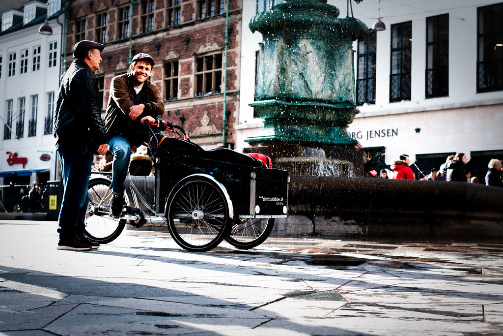 To mænd med ladcykel foran en springvand i en københavnsk gade